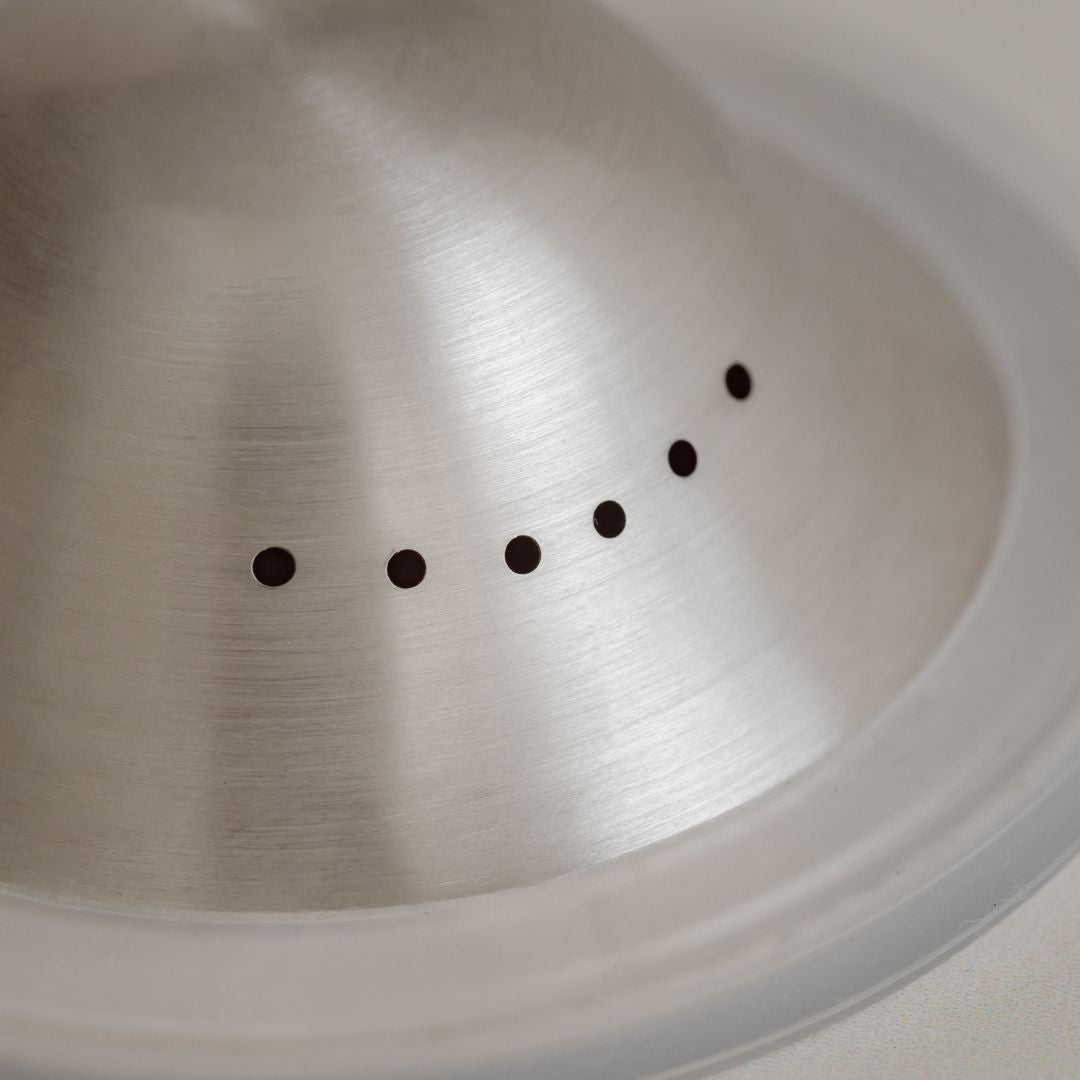 Close-up of a Mammae silver nipple cups surface with a series of small, spaced-out, circular perforations.