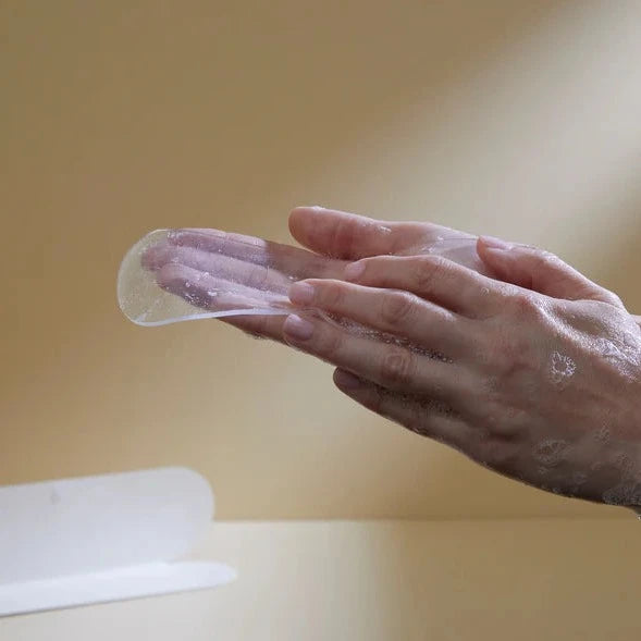 Hand applying Bare Mum Silicone Gel Scar Strips from a container against a soft beige background.