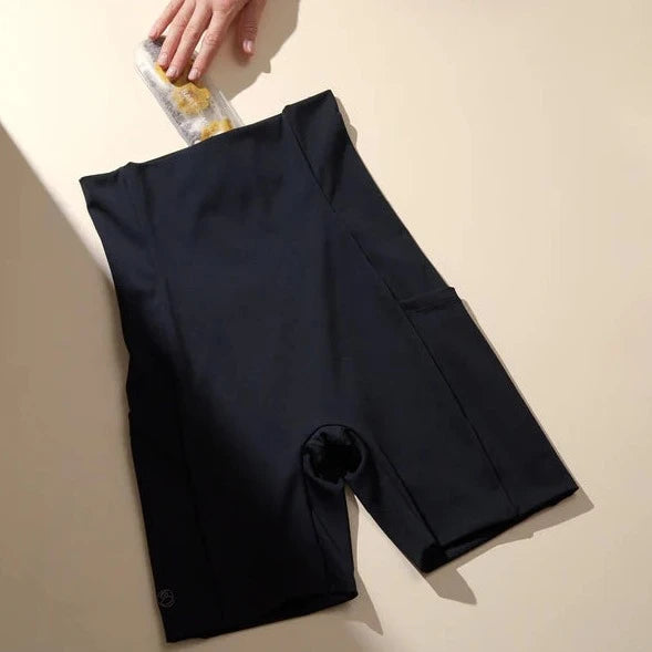 A hand pouring paint onto a dark fabric with the Bare Mum Postpartum Recovery Shorts with a 360Hold feature on a beige background, creating an artistic effect.