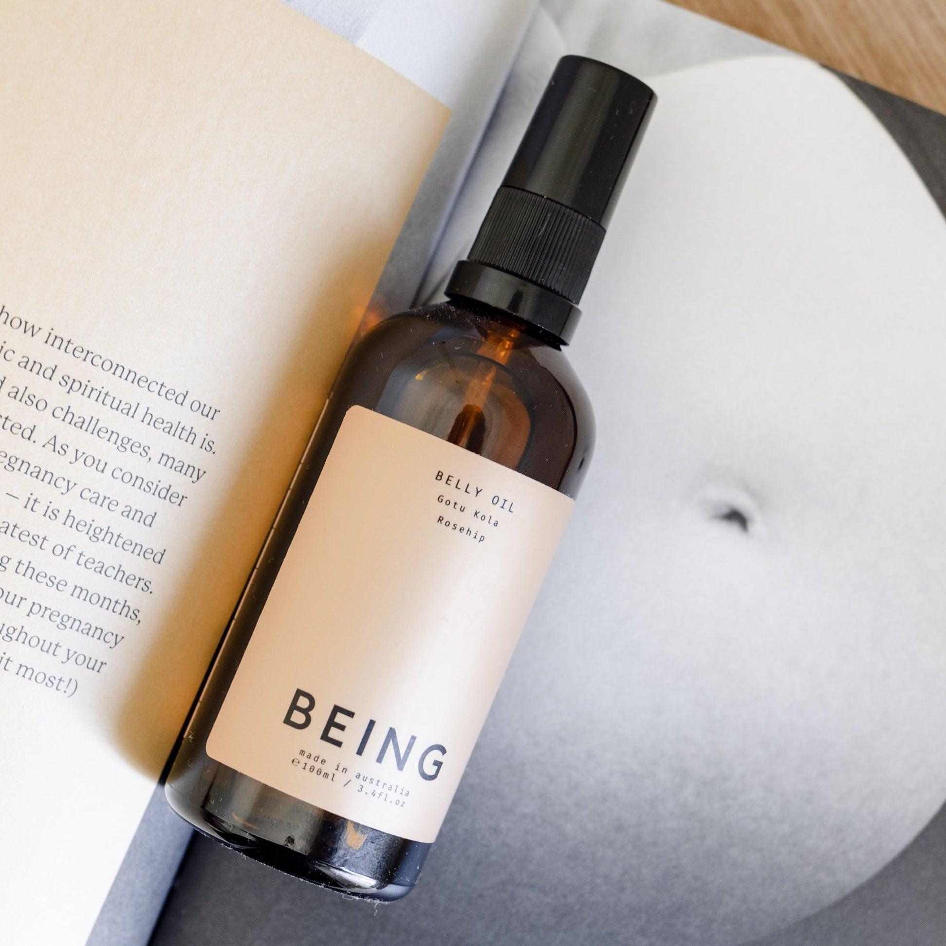 A bottle of Being Skincare Belly Oil next to a book.