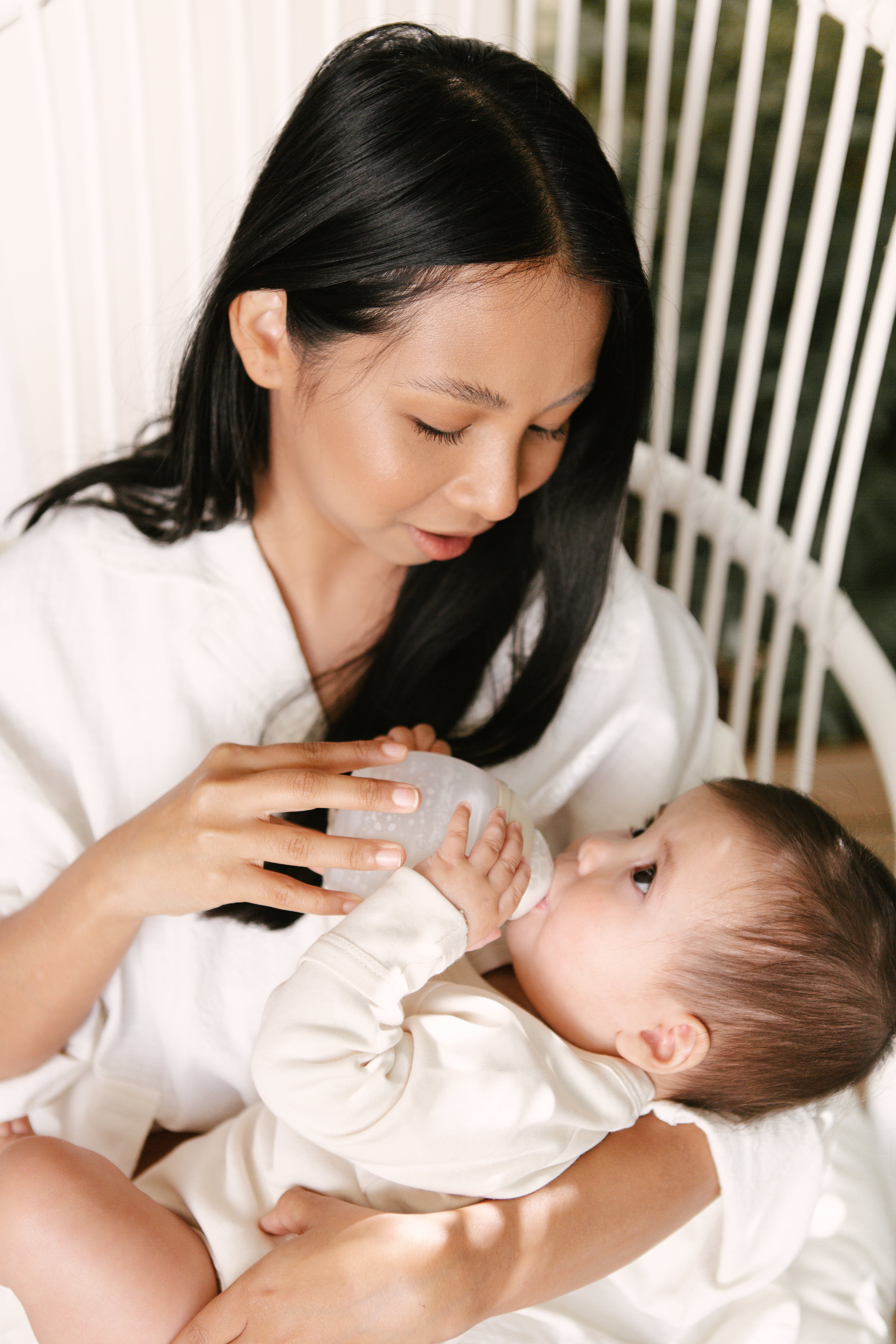 A woman is feeding a baby in a white chair.