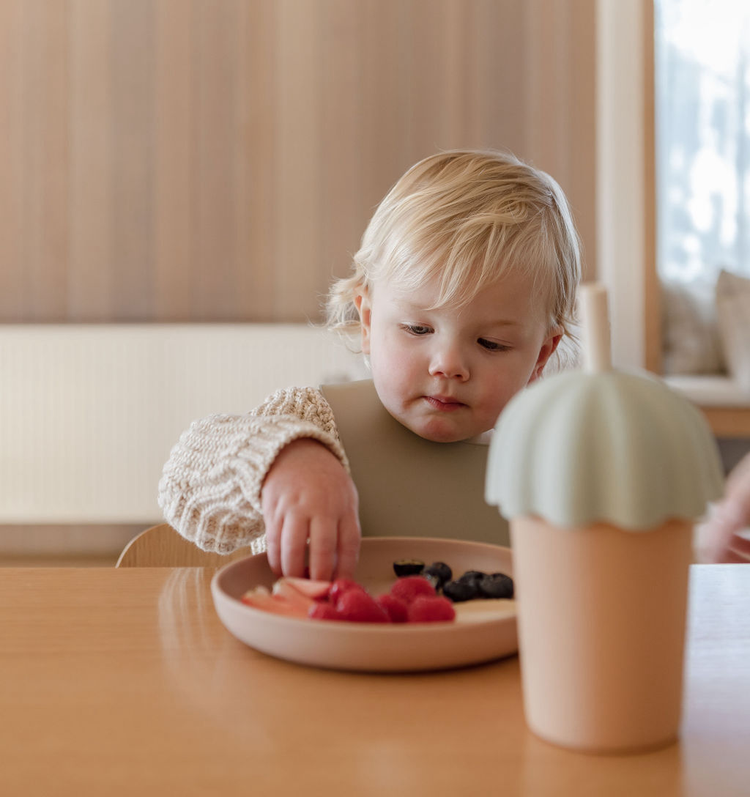 A child is eating food from a plate at a table.