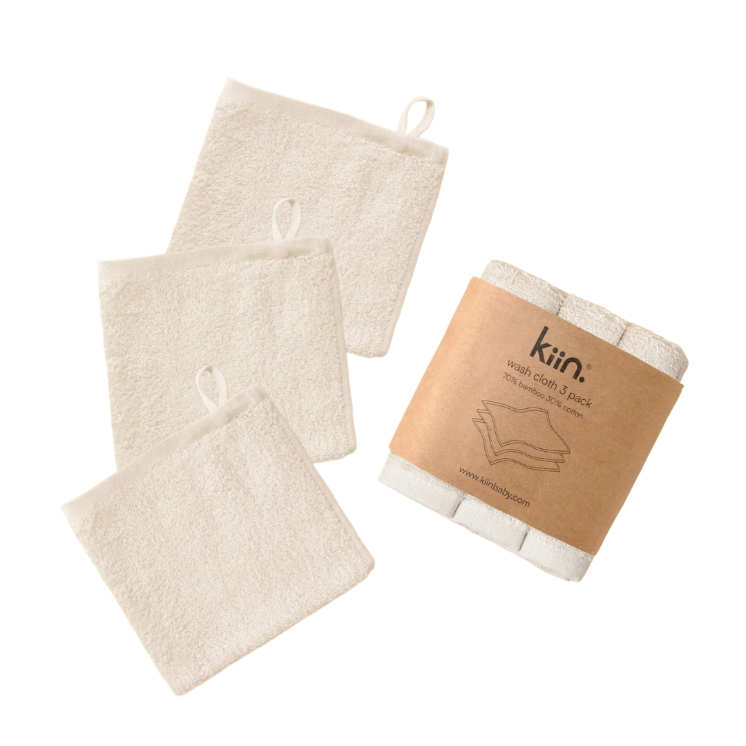 A set of four ivory washcloths, made from a 500gsm blend of cotton and bamboo, include handy hanging loops. While three lie flat, one is folded with a brown paper label that reads "Kiin Wash Cloth 3pk," making it an ideal addition to any bath and nappy change accessory collection.