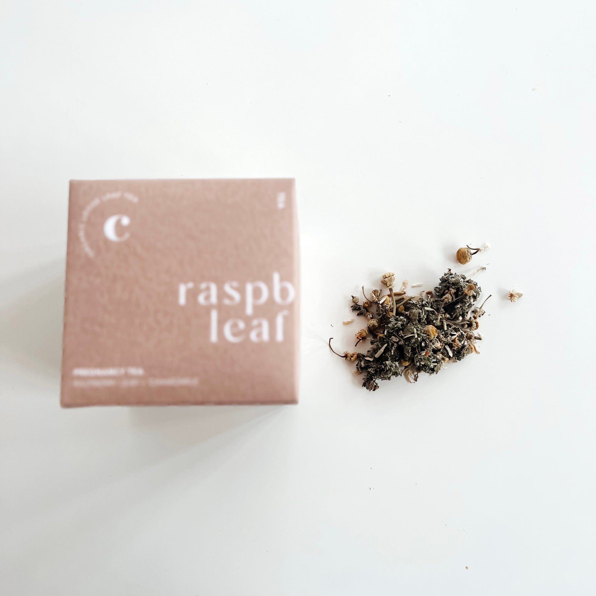 A box of Clē Naturals certified organic Raspberry Leaf Tea next to a pile of dried raspberry leaves on a white background.