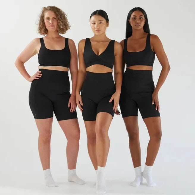 Three women in black Bare Mum postpartum recovery shorts standing together against a white background.